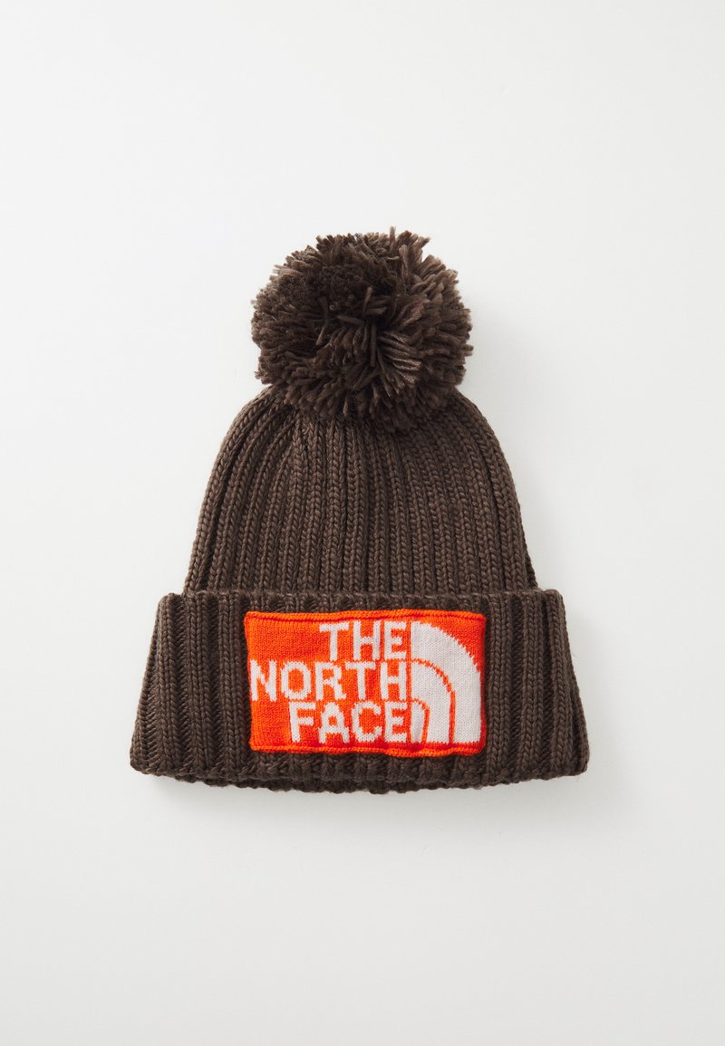 Brun strikket lue med en dusk på toppen. Har en oransje etikett med "THE NORTH FACE" i hvit tekst og en hvit logo.