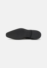 Semelle de chaussure habillée en cuir noir avec un motif de grip texturé, forme ovale allongée et talon légèrement surélevé pour plus de stabilit é.
