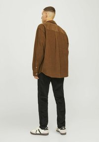 Chemise en velours côtelé marron à coupe décontractée avec un détail en empiècement au dos, associée à un pantalon noir et des baskets blanches.