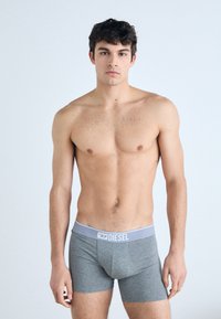 Boxer shorts gris en tissu doux, avec une ceinture contrastante portant le nom de la marque "DIESEL" en lettres grasses.