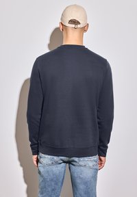 Navy blue sweatshirt with a crew neckline and ribbed cuffs, paired with light blue jeans. The fabric appears soft and textured.