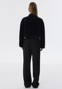 Zwarte cropped jas met contrasterende witte stiksels, gecombineerd met hoge taille zwarte broeken. Gladde textuur, eenvoudig ontwerp, geen zichtbare hardware.