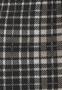 Tessuto a quadri nero e beige con grandi check caratterizzati da linee diagonali e una trama strutturata. Il design alterna quadrati solidi a quadrati con fantasia.