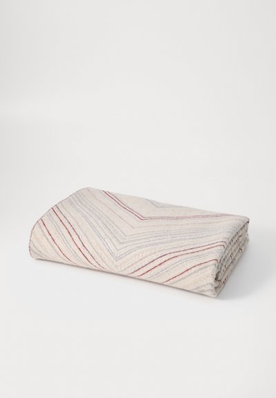 Pătură pliată cu o bază de crem, având un model în zigzag format din dungi albastre și bordeaux. Textură moale cu detalii tricotate vizibile.