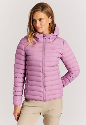 Vrouw draagt een lichtpaarse doorgestikte capuchonjas met beige broek, staat met één hand op haar heup tegen een effen achtergrond.