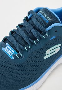Sininen verkkolenkkari, joka on kevyt, erottuva Skechers-logo ja tagi, joka ilmoittaa, että se on konepestävä. Rakeinen päällinen, jossa on rei'ityksiä.