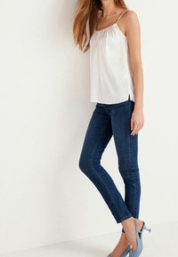 Hvid satinkjole med rund halsudskæring, parret med mørkeblå skinny jeans og lyseblå hælede sandaler. Enkel, tætsiddende design.