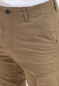 Khakifärgade cargobyxor med texturerad yta, som har flera fickor, en framknapp och en modern passform. Hållbart material med rutmönster.