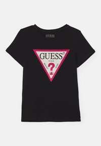 Schwarzes kurzärmliges T-Shirt aus Bio-Baumwolle. Mit einem dreieckigen Grafikdesign, dem "GUESS"-Logo, pinkem Rand und verziertem Fragezeichen.