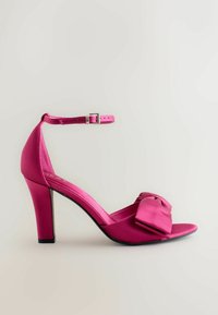 Scarpa con tacco alto in satin rosa, dotata di un fiocco sul davanti, cinturino alla caviglia regolabile e tacco a punta. Tessuto liscio con una finitura lucida.