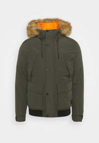 Giacca isolata verde oliva con cappuccio foderato in pelliccia, fodera interna arancione, due tasche frontali e polsini a coste, con chiusura a bottone a pressione.