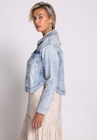 Hellblaue Jeansjacke in kurzer Länge mit klassischem Kragen, Knopfleiste vorne und zwei Brusttaschen. Verfügt über eine ausgewaschene Textur und einen ausgefransten Saum.