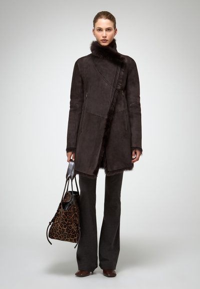 Palton din suede maro cu guler de blană, buzunare cu fermoar și un design asimetric. Asortat cu pantaloni evazați închiși la culoare și o geantă cu imprimeu leopard.
