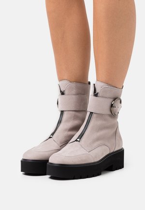 Des bottines en cuir gris pour la cheville comportent une fermeture éclair sur le côté, une semelle robuste et une sangle décorative avec boucle. Le design combine des finitions texturées et lisses.