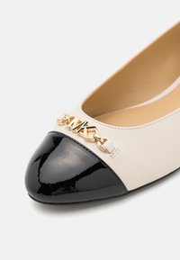 Klassiset ballerinat vaaleassa nahassa, jossa on musta lakkapintainen kärki. Yksityiskohtana kultaketju avautumiskohdassa. Silkkisen sileä pinta.
