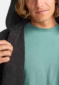 Black zip-up jacket with a soft, textured fleece lining, worn over a solid teal T-shirt. The jacket features a hood and is partially open.