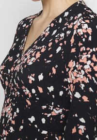 Svart klänning med V-ringning, med ett färgglatt abstrakt mönster i persika och vitt. Mjuk tyg, något strukturerad, med lång ärm.