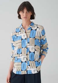 Camicia a maniche lunghe abbottonata in una miscela di colori crema, blu e nero. Presenta un audace motivo geometrico con varie forme e texture.