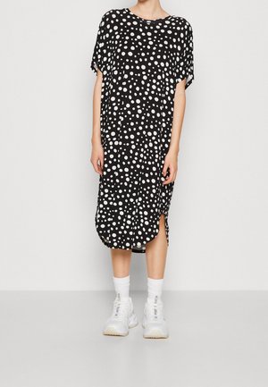 Robe noire à pois blancs, manches courtes, décolleté rond, fentes latérales, longueur genou, associée à des baskets blanches et des chaussettes.