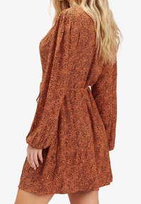Robe à manches longues, longueur genou en orange avec un imprimé animal noir. Elle présente une taille cintrée et des manches froncées pour un ajustement décontracté.