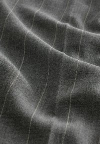 Donkergrijze stof met een zachte textuur, voorzien van subtiele lichtgrijze strepen die verticaal lopen en een patroon over het materiaal creëren.