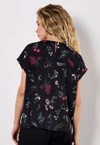 Blouse noire à fleurs avec manches courtes, coupe décontractée et détail en forme de clé à l'arrière. Le tissu présente divers motifs de fleurs colorées.
