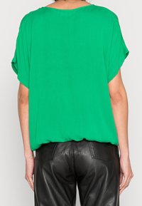 Haut léger vert avec des manches dolman courtes, texture lisse et coupe ample. Associé à un pantalon en cuir noir.