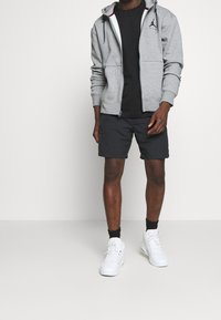 Szara bluza z kapturem na suwak, czarna koszulka, ciemne szorty i białe buty sportowe. Gładki materiał z przednimi kieszeniami i czarnymi akcentami.