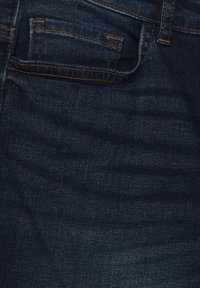 Jeans de mezclilla azul oscuro con un diseño clásico de cinco bolsillos. Presentan costura naranja en contraste y una tela suave, ligeramente texturizada.