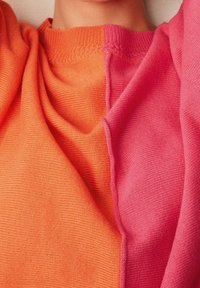 Suéter de punto con diseño dividido en tonos naranja y rosa, que muestra una textura suave y un cuello acanalado.