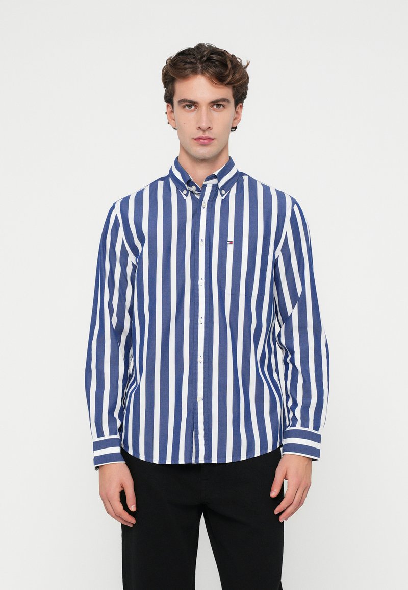 Μπλε και λευκή ριγέ πουκάμισο με κουμπιά, φτιαγμένο από βαμβάκι, που διαθέτει γιακά, μακριά μανίκια και μία τσέπη στο στήθος με μια μικρή λεπτομέρεια λογότυπου.