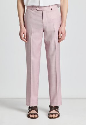 Pantalon rose clair sur mesure porté avec des sandales marron foncé à brides croisées et une chemise blanche rentrée.