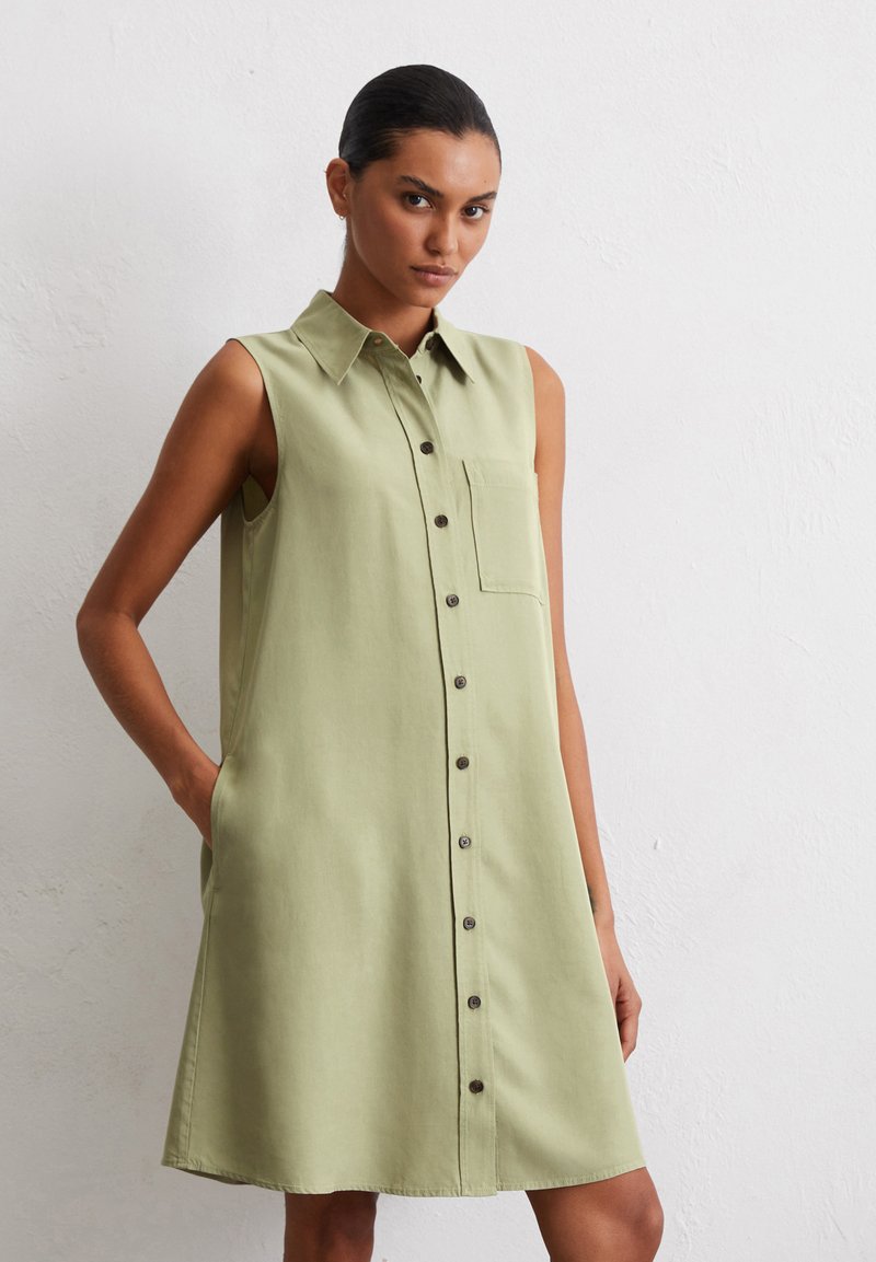 Robe sans manches, verte claire, avec un col, des boutons sur le devant et une poche poitrine ; fabriquée en tissu doux avec une texture lisse.