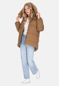 Bruine pufferjack met een grote capuchon, voorzien van gestikte delen. Draag over een wit topje en lichte blauwe jeans, gecombineerd met witte sneakers.