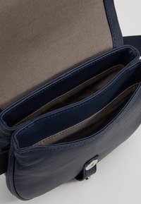 Granatowa skórzana torba na ramię z dwoma wewnętrznymi przegrodami, gładką fakturą i zapięciem na srebrny zatrzask. Podszewka z jasnej tkaniny.