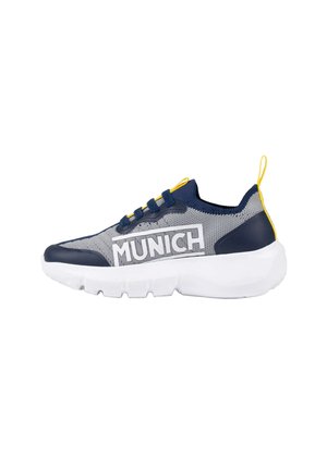 Zapatilla deportiva baja en malla gris con detalles en azul marino y amarillo, suela blanca gruesa y marca "MUNICH" en el lateral.