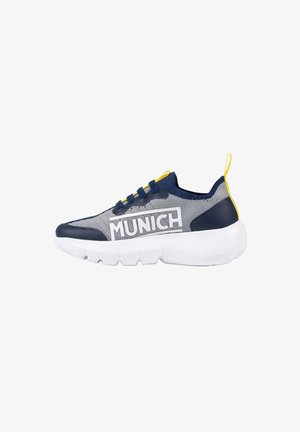Zapatilla deportiva baja en malla gris con detalles en azul marino y amarillo, suela blanca gruesa y marca "MUNICH" en el lateral.