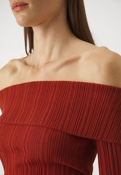 Off-the-shoulder, ribbed top in deep red. Features vertical pleats, a fitted silhouette, and a smooth texture. Sleek, minimalist design.