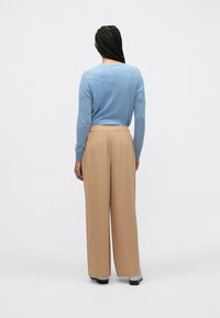 Ανοιχτό μπλε πουλόβερ με μακριά μανίκια, συνδυασμένο με μπεζ παντελόνια φαρδιάς γραμμής με ελαστική μέση. Ομαλή υφή με άνετη εφαρμογή.