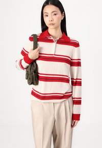 Red and white striped long-sleeve polo sweater with a red ribbed collar, paired with beige wide-leg trousers and a green shoulder bag.