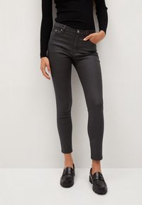 Jeans de talle alto negros con un ajuste ceñido, que presentan bolsillos frontales y una textura suave y brillante, combinados con mocasines negros.