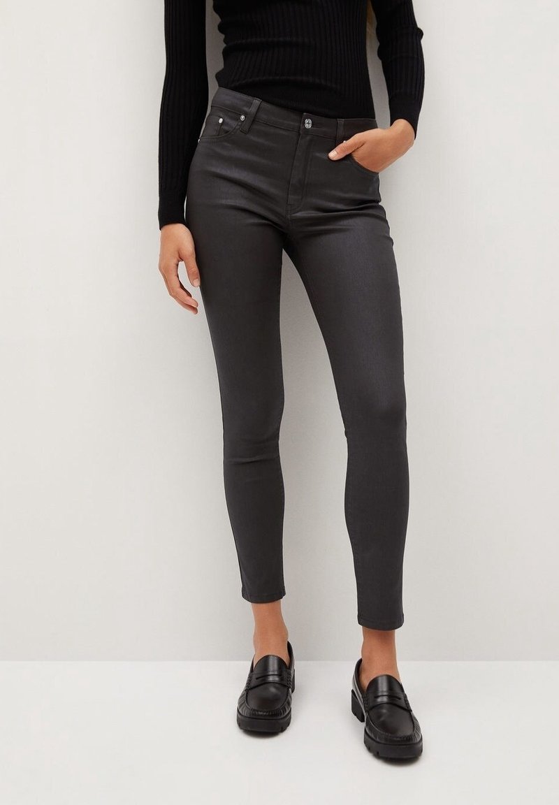 Jeans de talle alto negros con un ajuste ceñido, que presentan bolsillos frontales y una textura suave y brillante, combinados con mocasines negros.