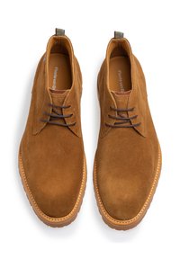 Bottines en daim marron à surface texturée, bout rond et fermeture à lacets. Comprend une languette à rayures et une semelle en caoutchouc contrastante.