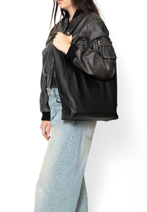 Sac fourre-tout en cuir noir avec une finition texturée, de forme rectangulaire et avec un matériel minimal, présenté sur un fond blanc.