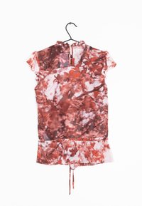 Blouse transparente à manches courtes avec un col volanté dans un motif abstrait rouge et rose. Dispose d'un lien en bas et d'une fermeture à boutons dans le dos.