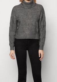 Suéter de punto gris con cuello alto, patrón texturizado, puños y dobladillo acanalados, de longitud corta, combinado con jeans negros.