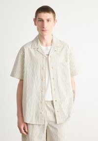 Short-sleeved, button-up shirt in cream with navy vertical stripes. Features a chest pocket and is made of lightweight fabric.
