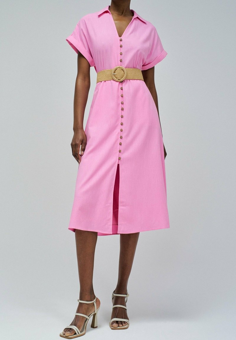 Robe rose à manches courtes, avec une ceinture à la taille et une fente à l'avant. Présente une coupe décontractée et un tissu texturé. Conception avec un col ouvert.