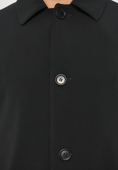 Zwarte jas met een gladde matte afwerking, voorzien van een puntige kraag en twee zwarte knopen. Minimalistisch ontwerp met strakke lijnen en subtiele stiksels.