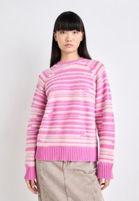 Pull en tricot rayé rose et crème avec un col ras du cou, des bords côtes aux poignets et à l'ourlet. Texture plus douce avec des rayures inégales pour un intérêt visuel.